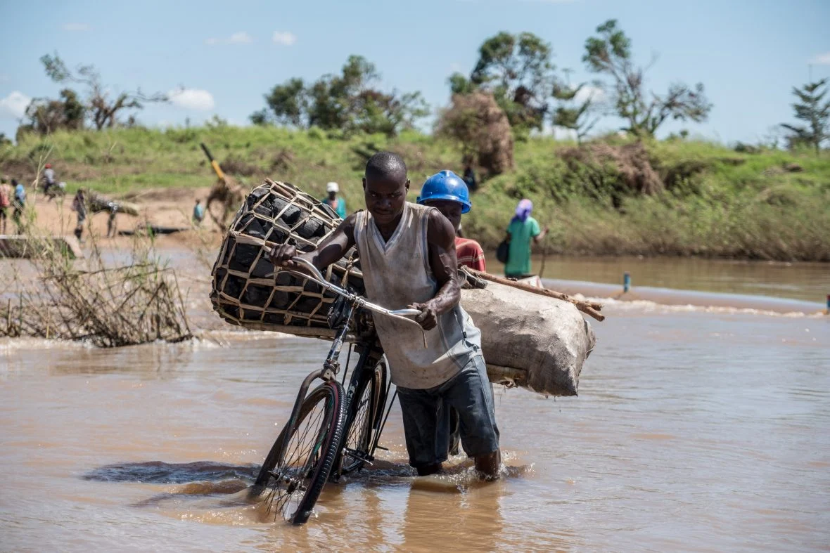 Zaccharia Roberto pushes his bicycle laden with charcoal across a flooded river near Nhamatanda, Mozambique. In 2019, Cyclone Idai disrupted infrastructure across the country, impacting livelihoods and hampering aid efforts. (Photo: Tommy Trenchard/Concern Worldwide)