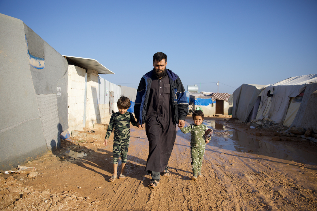 Jaafar* (32) walks with his children on the muddy roads of the Ahl al-Khair camp, which was established after the February 6th 2023 earthquake. (Photo: Ali Haj Suleiman/DEC/Fairpicture)
