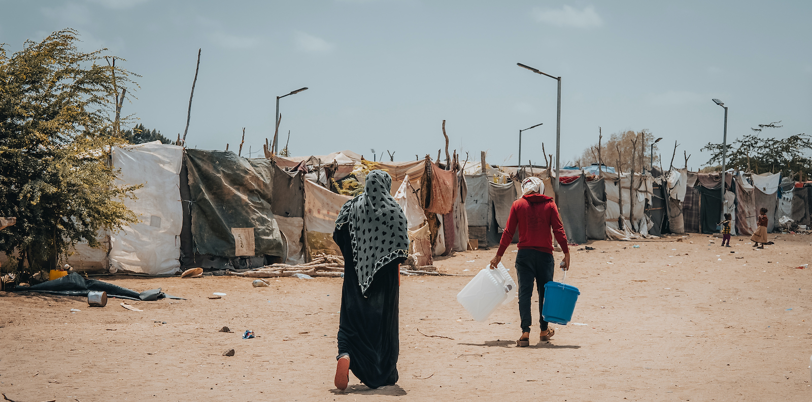 A mother and children returning to her tent within camp after receiving her cholera/hygiene kit, Al-Salam City IDP camp, Dar Saad district, Aden Governorate. (Photo: Ammar Khalaf/Concern Worldwide)