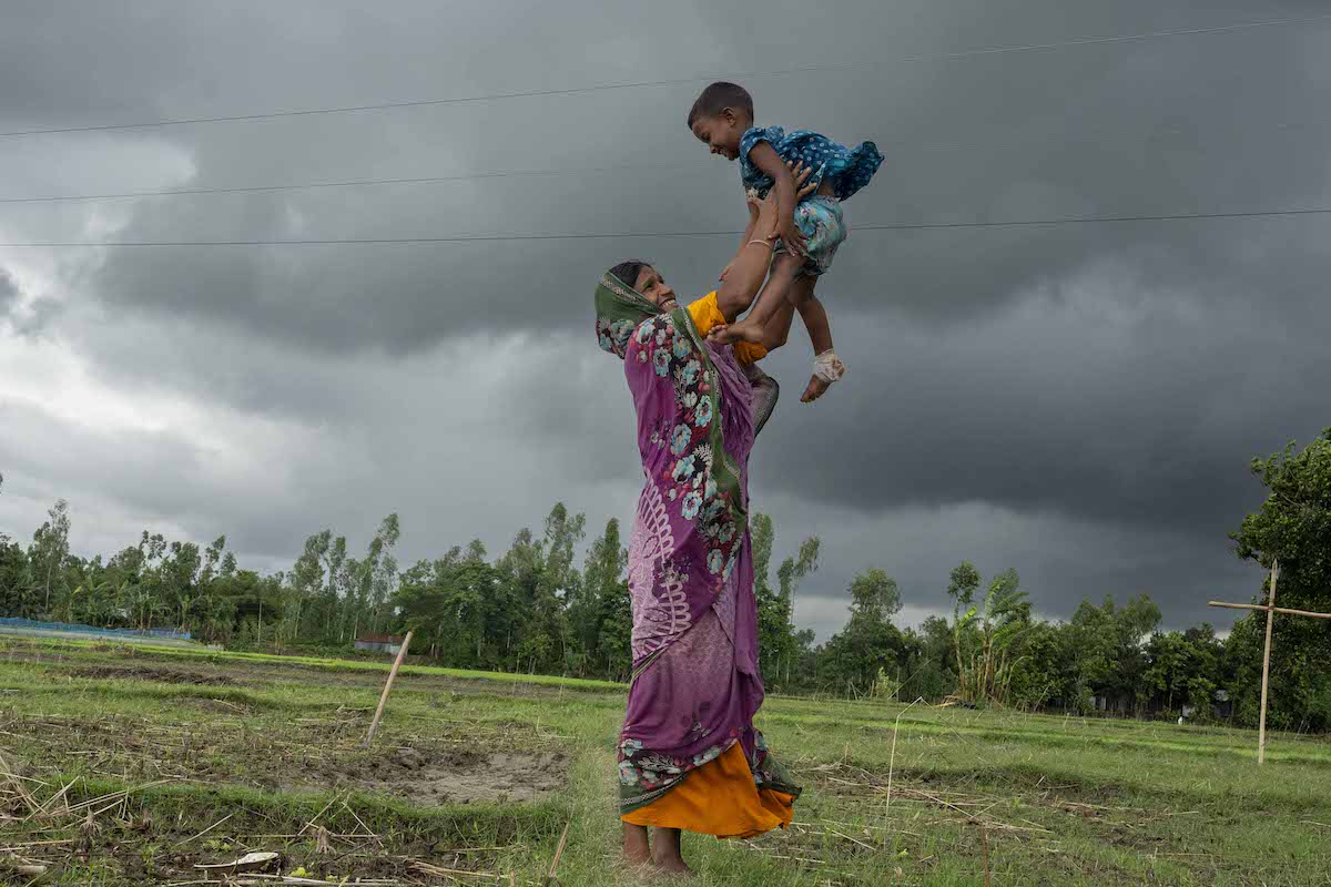 Mst. Sumi Begum (26), lifts her daughter Hia Moni (3). Once displaced by flooding, Sumi's family has now returned here to their native village in Charitabari in Sundarganj, thanks to the flood-resistant housing implemented by Gana Unnayan Kendra, with the support of Concern Worldwide. Photo: Saikat Mojumder/Concern Worldwide