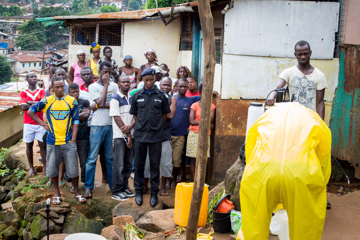 Community members look on as Concern Worldwide’s Burial Team 7 attends the home of a 44-year-old woman in Freetown who has recently died, likely from Ebola. (Photo: Kieran McConville/Concern Worldwide)