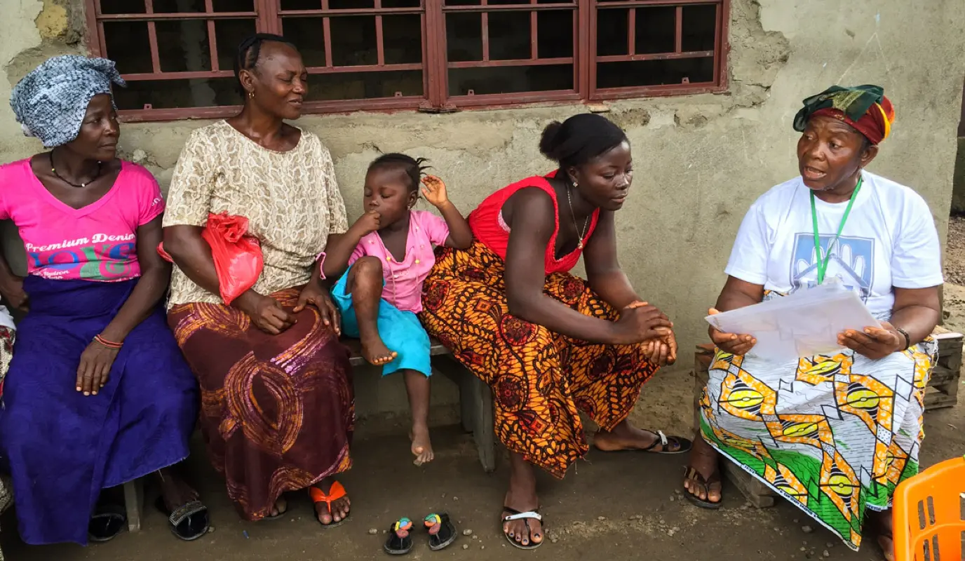 Kai Giba, a health promoter, uses pictorial cards to teach families good health practices during a home visit.