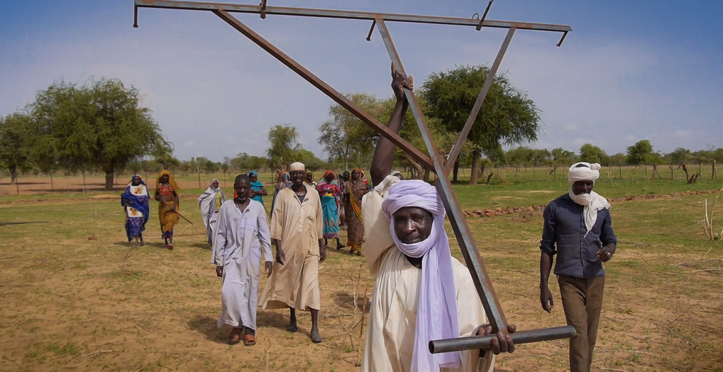 A man carries a planting tool in an open field.