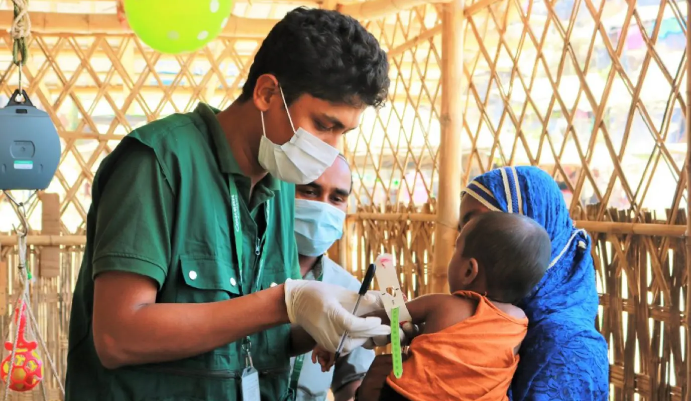 Man in medical mask assesses child.